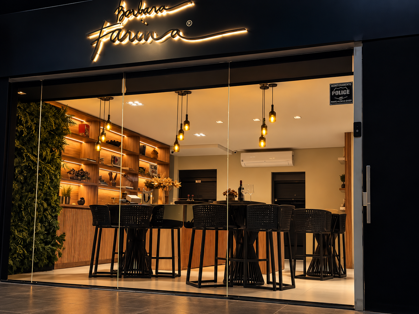 Fachada da loja Bárbara Farina à noite, com letreiro iluminado e salão aconchegante